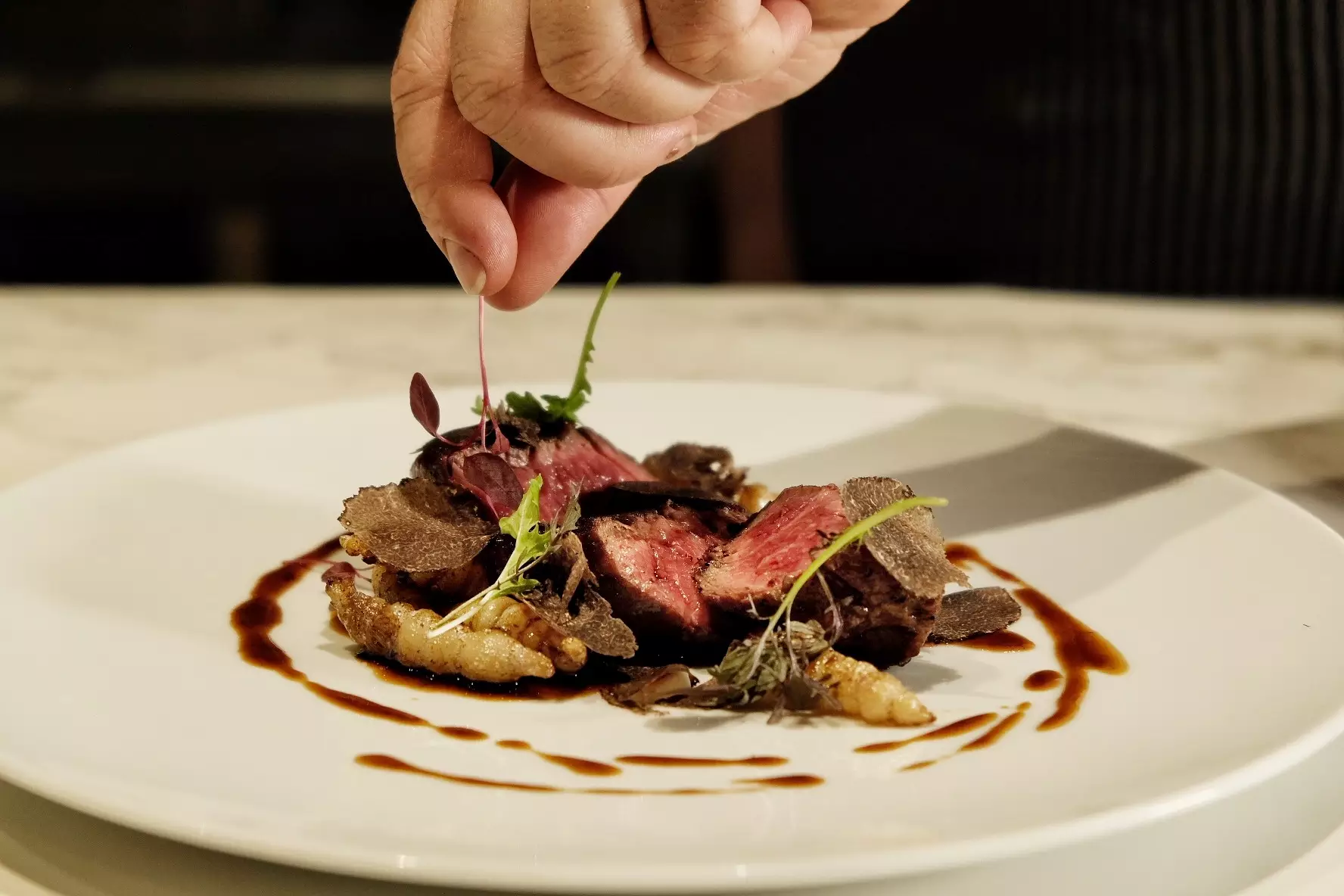 Mano colocando brotes en un plato de carne