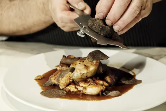 Primer plano de unas manos mientras rallan trufa sobre un plato de pescado